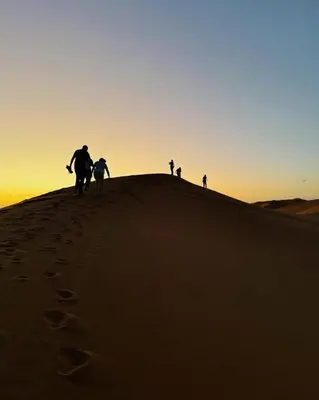 people walking on top of a sand hill in the desert at Golden Sahara camp in Merzouga