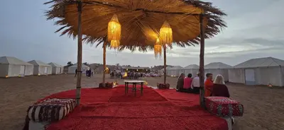 a group of people sitting under an umbrella on the beach at Touaregs Camp Erg Lihoudi in Mhamid