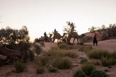 a group of people riding camels in the desert at Touaregs Camp Erg Lihoudi in Mhamid