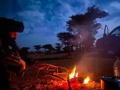 a person standing next to a fire with a car in the background at Private Wild Tent Experience M'Hamid in Mhamid
