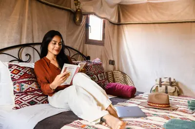 a woman sitting on a bed reading a book at Luxury beldi camp in Merzouga