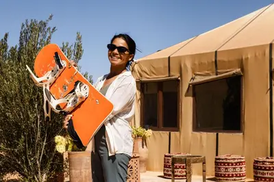 a woman holding a skateboard in front of a house at Luxury beldi camp in Merzouga