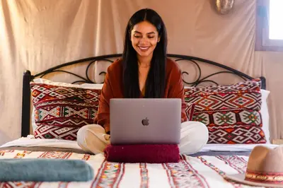 a woman sitting on a bed with a laptop at Luxury beldi camp in Merzouga