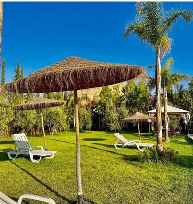a straw umbrella and two chairs and a palm tree at Tasnim VILLA in Marrakech