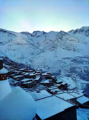 a village covered in snow with mountains in the background at Gîte Assonfo Tachdirt in Tacheddirt