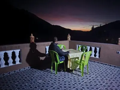 a man sitting at a table on a balcony at night at Gîte Assonfo Tachdirt in Tacheddirt
