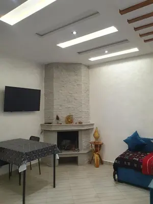a living room with a fireplace and a table and a tv at Guest house in Imouzzer Kandar