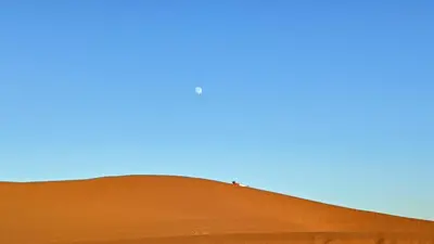 a person standing on top of a red sand dune at Akwabir camp in El Gouera