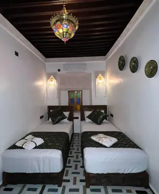 two beds in a room with a chandelier at Dar derb el miter in Fès