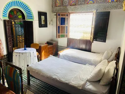 a bedroom with two beds and a table and a window at Fes Antique Hostel in Fès