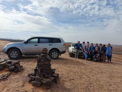 a group of people standing next to a car in the desert at hostel sable dor merzouga in Merzouga