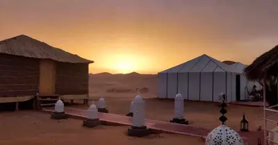 a group of tents in the desert with the sunset at jumeirah resort luxury desert camp in Merzouga