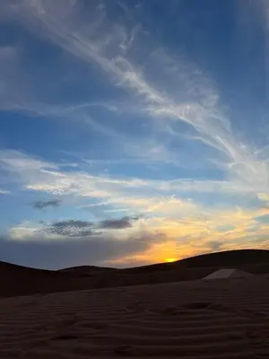 a sunset in the desert with the sun in the sky at Across Sahara in Bou Nou