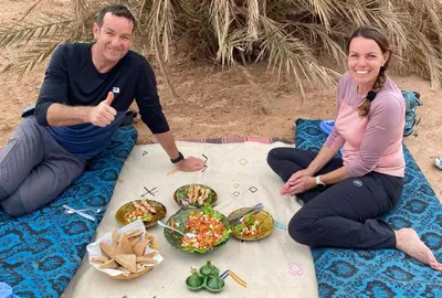 a man and a woman sitting on the beach with food at Across Sahara in Bou Nou