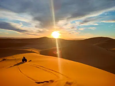 a person riding a motorcycle in the desert at sunset at Quiet Luxury Camp in Merzouga