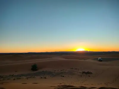 a car driving through the desert at sunset at Quiet Luxury Camp in Merzouga