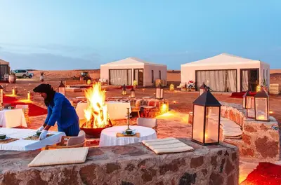 a person in a desert with tents and a fire at Quiet Luxury Camp in Merzouga