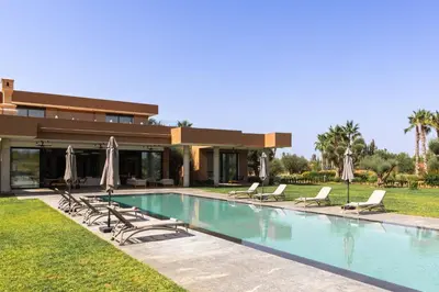 a pool with chairs and umbrellas in front of a house at Villa Dar Tillili Marrakech in Heddad