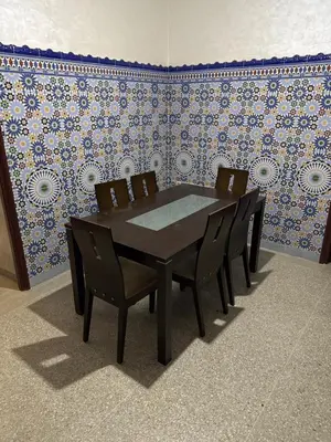 a table and chairs in a room with a wall at Bel appartement familial au centre ville in El Kelaa des Srarhna