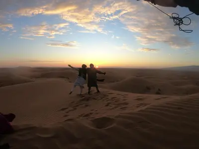 a couple standing on top of a sand dune in the desert at Sahara Dream Camp in Oulad Hammou