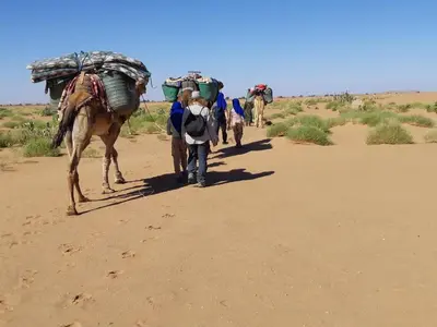 a group of people walking down a dirt road with a camel at Sahara Dream Camp in Oulad Hammou