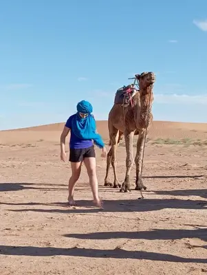a woman standing next to a camel in the desert at Sahara Dream Camp in Oulad Hammou