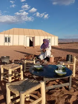 a man sitting in front of a tent in the desert at Sahara Dream Camp in Oulad Hammou
