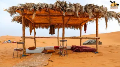 a bed in the desert with two chairs and a hut at sahara camp in Oulad Akkou