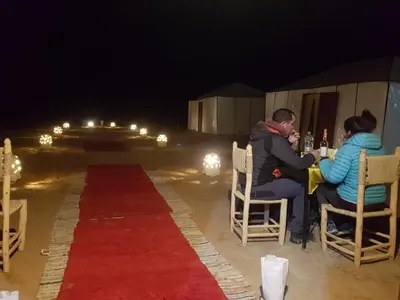 a man and woman sitting at a table at night at Merzouga Nomade Desert Camp in Merzouga