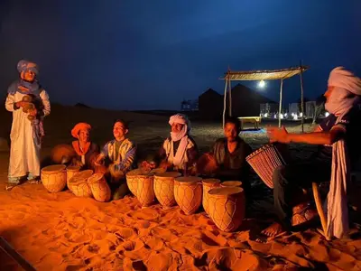 a group of people sitting on the beach at night at Merzouga Nomade Desert Camp in Merzouga