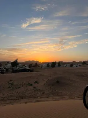 a sunset in the desert with a house in the distance at Finest Luxury Camp in Merzouga