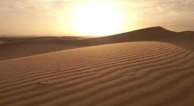 a sand dune with the sun in the background at jumeirah standard camp merzoug in Merzouga