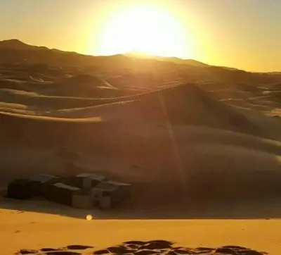 a desert with the sun rising over a mound of sand at jumeirah standard camp merzoug in Merzouga