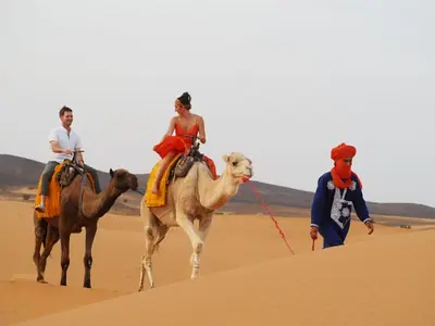 three people riding on camels in the desert at Gnaoua Luxury Camp in Merzouga