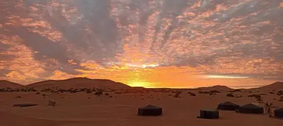 a sunset in the desert with tents in the sand at Gnaoua Luxury Camp in Merzouga