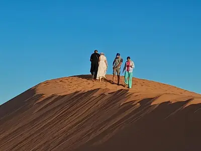 three people standing on top of a sand dune at Gnaoua Luxury Camp in Merzouga