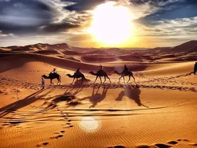 a group of people riding camels in the desert at Gnaoua Luxury Camp in Merzouga