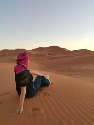a woman sitting on the sand in the desert at Gnaoua Luxury Camp in Merzouga