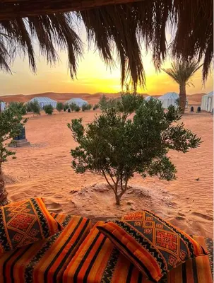 a bed in the desert with a sunset in the background at Happy luxury camp in Merzouga