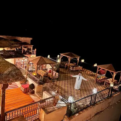a man in a robe standing on a deck at night at Ecolodge Dar itran in Azilal