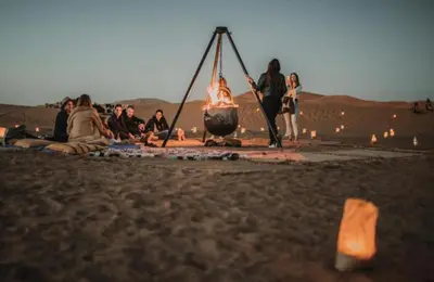 a group of people sitting around a fire in the desert at Merzouga appartements in Merzouga