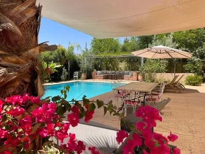 a swimming pool with a table and some pink flowers at Dar Muezza in Marrakech