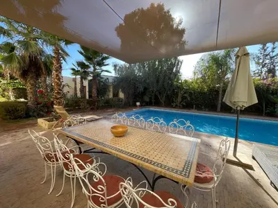 a table with chairs and an umbrella next to a pool at Dar Muezza in Marrakech