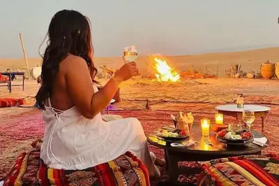 a woman sitting in front of a table with a wine glass at Marruecos Excursiones Camp in Mezguida