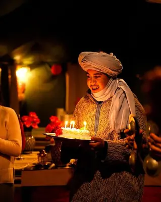 a woman holding a cake with lit candles on it at Merzouga Sahara Top Camp in Merzouga