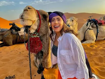 a woman standing next to a camel in the desert at Merzouga Sahara Top Camp in Merzouga
