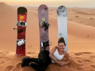 a woman sitting in the desert with two snowboards at Merzouga Sahara Top Camp in Merzouga