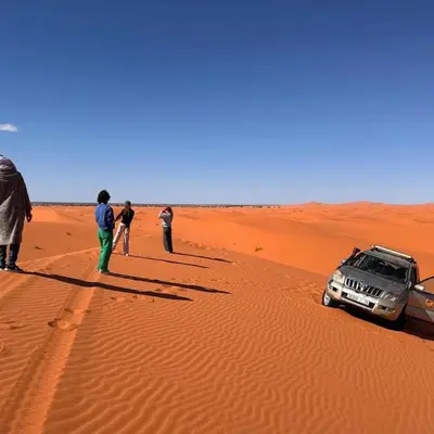 a group of people standing next to a car in the desert at Tipic luxury camp in Merzouga
