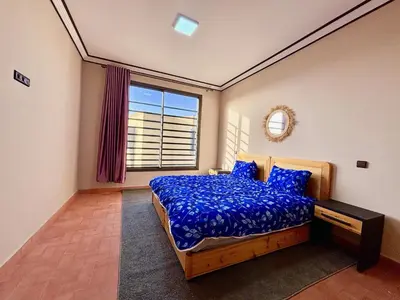 a bedroom with a bed with a blue comforter and a window at Complexe Kariat Ayoub in Aït Zat