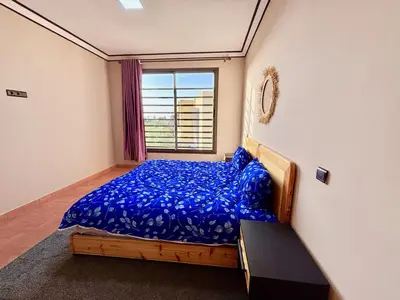 a bedroom with a bed with blue sheets and a window at Complexe Kariat Ayoub in Aït Zat